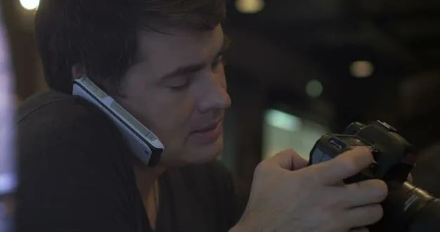 A close-up shot of a filmmaker using a smartphone as a camera in a dimly lit indoor setting, showcasing the resourcefulness of using readily available technology in micro-budget filmmaking.