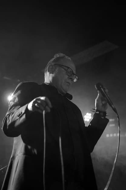 A black and white portrait of Ennio Morricone conducting an orchestra, capturing his passion and intensity. The lighting is dramatic to emphasize his facial expressions and gestures.