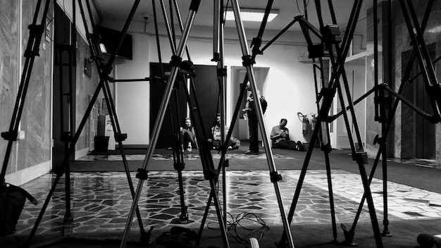 A behind-the-scenes photograph of a film crew setting up a forced perspective shot. The image shows the careful arrangement of props and actors to create the illusion of depth and distance.