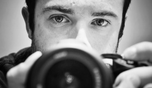 A close-up shot of a director looking through the camera lens on a film set, with the focus on their eye and the camera.