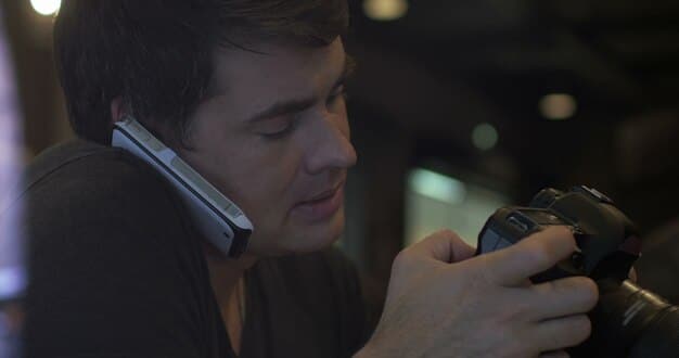 A close-up shot of a filmmaker using a smartphone as a camera in a dimly lit indoor setting, showcasing the resourcefulness of using readily available technology in micro-budget filmmaking.