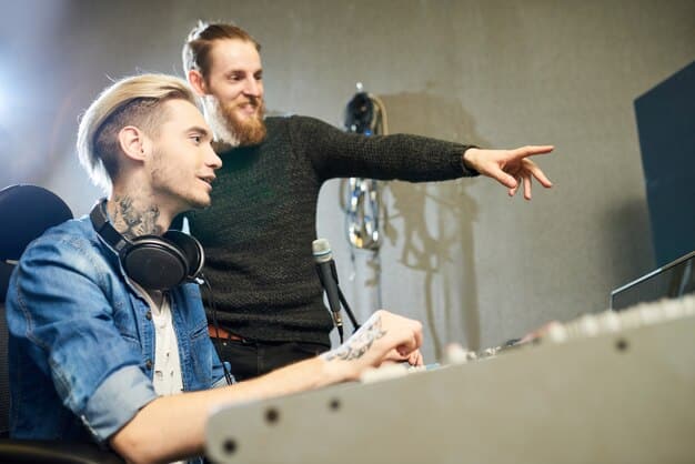 Two musicians collaborating in a recording studio, one playing a keyboard and the other giving direction while looking at a screen with film editing software.