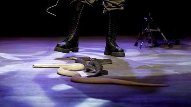 A scene from the film showing the band Spinal Tap getting lost backstage in a large concert venue. They are surrounded by stagehands and props, and their expressions show frustration and confusion.